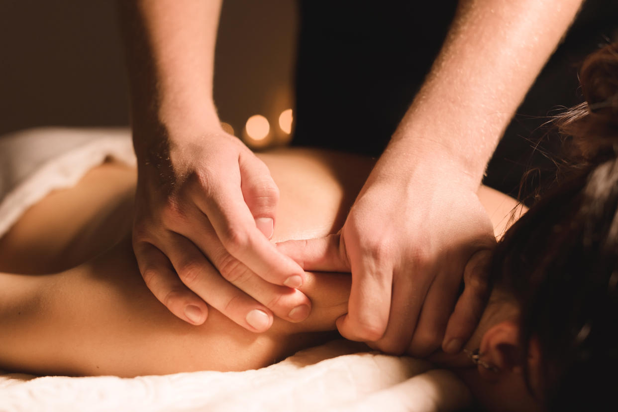 Men's hands make a therapeutic neck massage for a girl lying on a massage couch in a massage spa with dark lighting. Close-up. Dark Key.