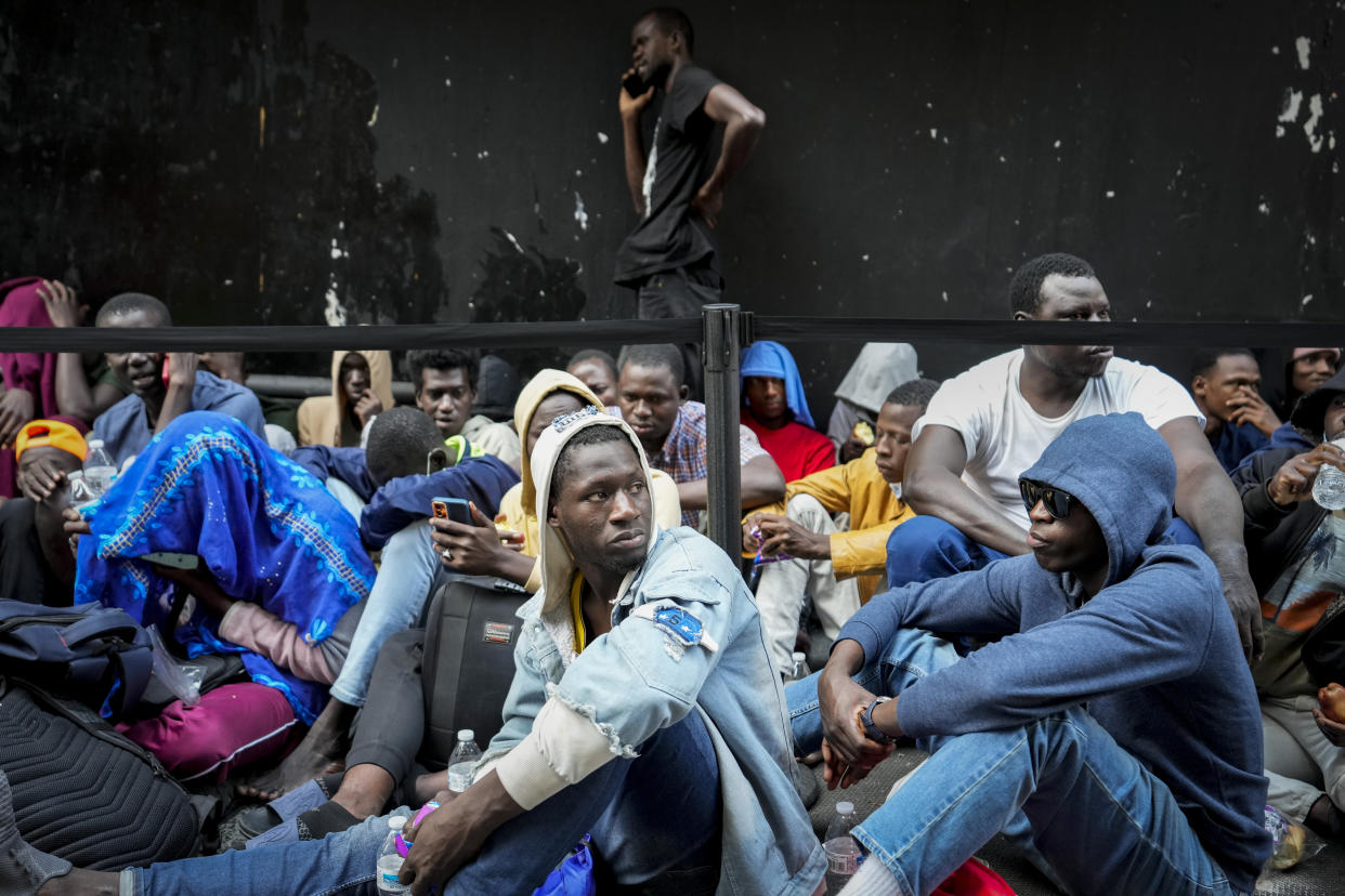 Migrants in hoodies seated on the ground.