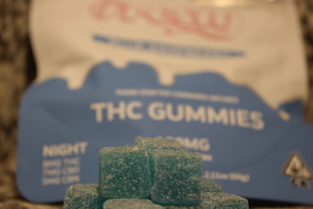 Edible THC gummies stacked in foreground of package labeled "Blue Raspberry" flavor