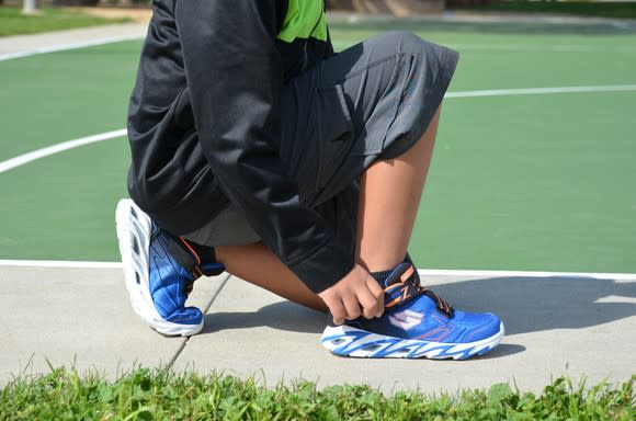 Someone adjusting his shoes at an outdoor basketball court.