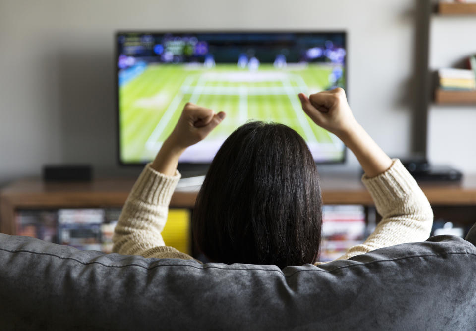 Young woman watching tennis on TV and cheering