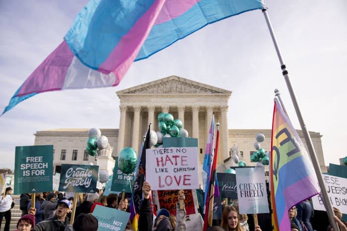 Protesters wave pride flags, trans pride flags, and signs that read "there's no hate like Christian love" and "free speech is for everyone"