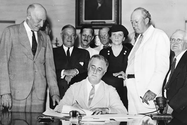 President Franklin D. Roosevelt signs the Social Security Act into law at the White House on August 14, 1935. On March 4, 1933, Frances Perkins, standing behind FDR, was sworn in as U.S. labor secretary, becoming the first female member of the Cabinet. File photo by ACME Newspictures