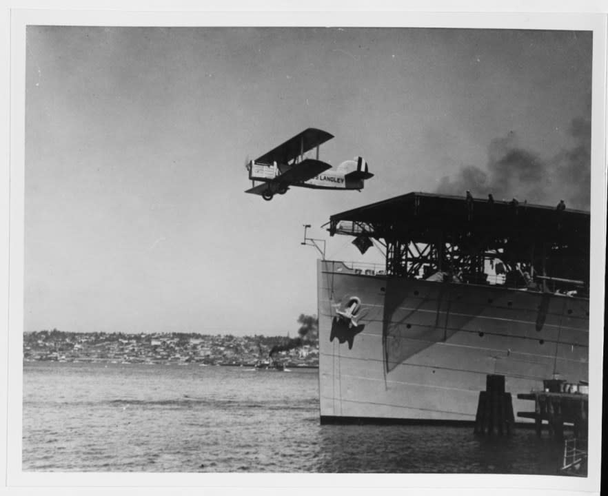 Docked at the carrier pier at Naval Air Station, North Island, San Diego, California, with a Douglas DT-2 airplane taking off from her flight deck. This photo may have been taken during catapult tests in 1925. (NHHC)