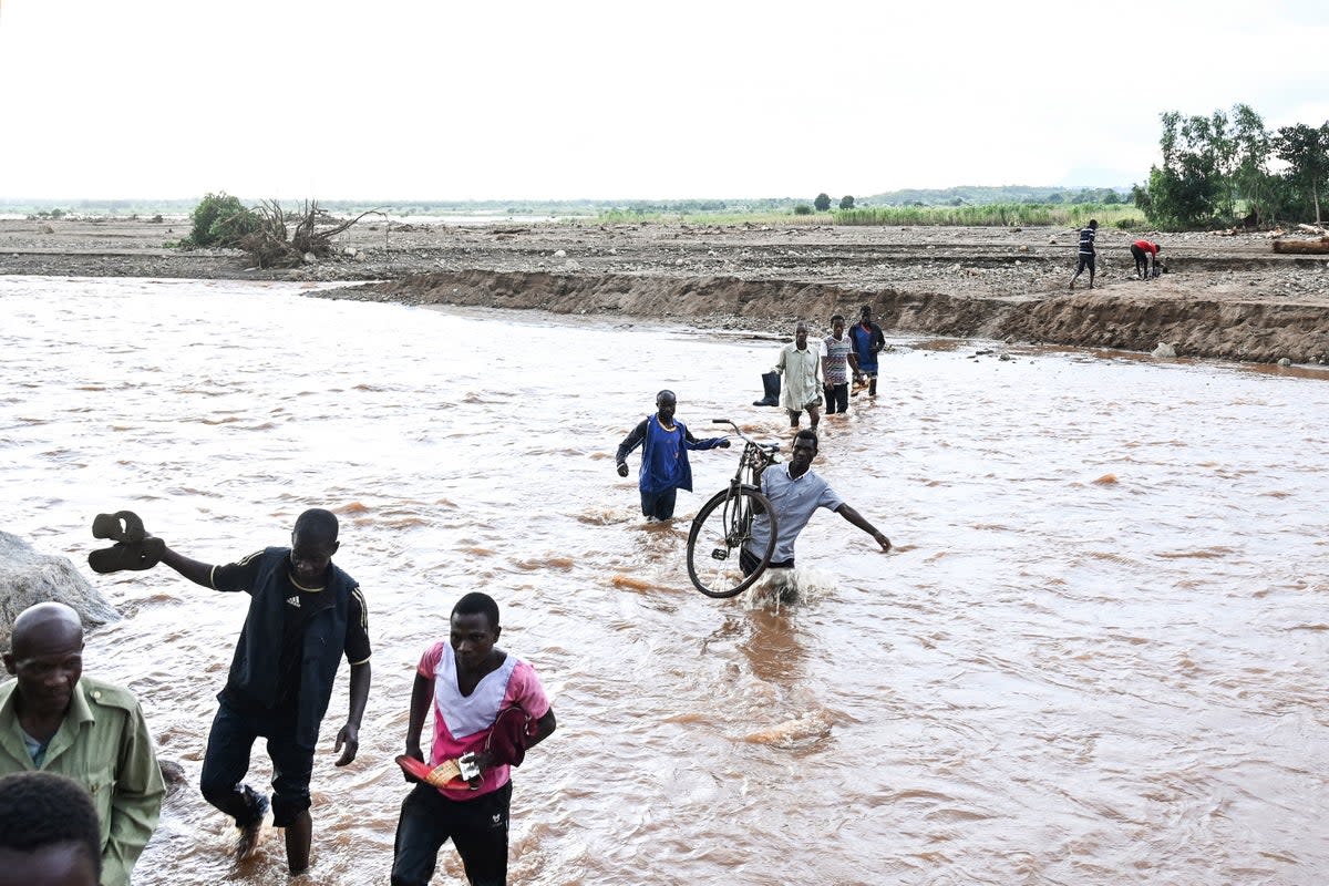 People wade through flood waters caused by last week’s heavy rains caused by Tropical Cyclone Freddy in Phalombe, southern Malaw (AP)