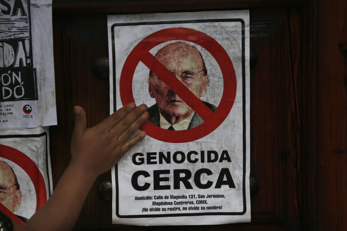 A protester places a poster with a message that reads in Spanish, "Genocide near you," with an image of former Mexican President Luis Echeverría, on the front gate of his residence, during a march to commemorate the 50th anniversary of the student massacre of 1971 known as "El Halconazo," in Mexico City, Thursday, June 10, 2021. The attack, also known as the Corpus Christi massacre, was carried out by a group of men apparently recruited by the government to dissolve a pro-democracy student demonstration. (AP Photo/Marco Ugarte)