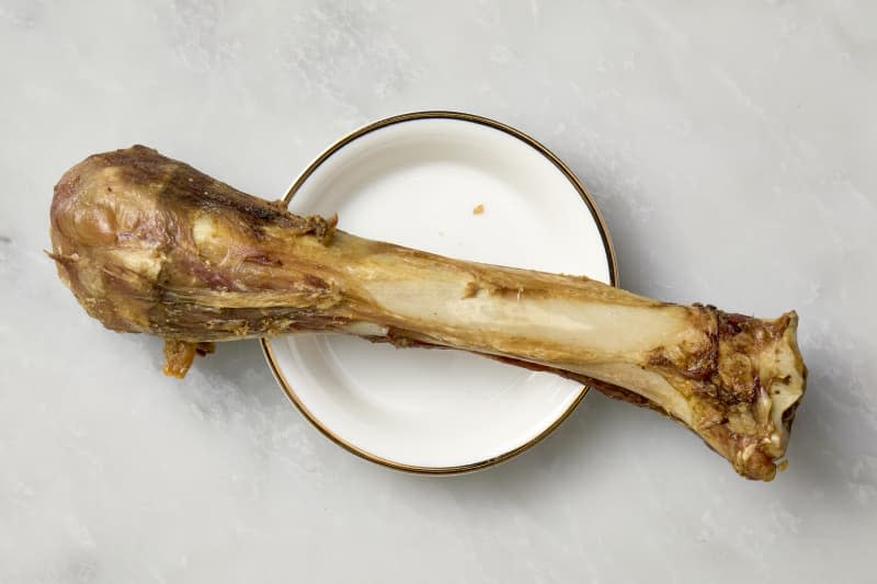 overhead shot of a shank bone on a small white plate with a gold rim.