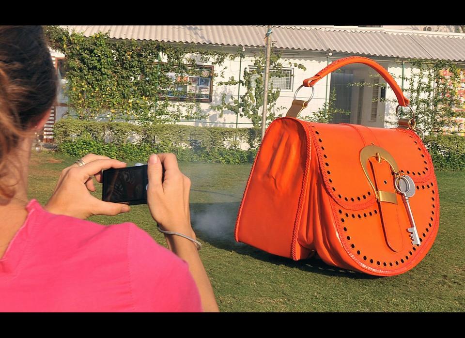 A woman takes a video on her mobile phone of Indian wacky car designer Sudhakar Yadav (unseen) driving a vehicle made in the shape of Ladies Hand Bag.