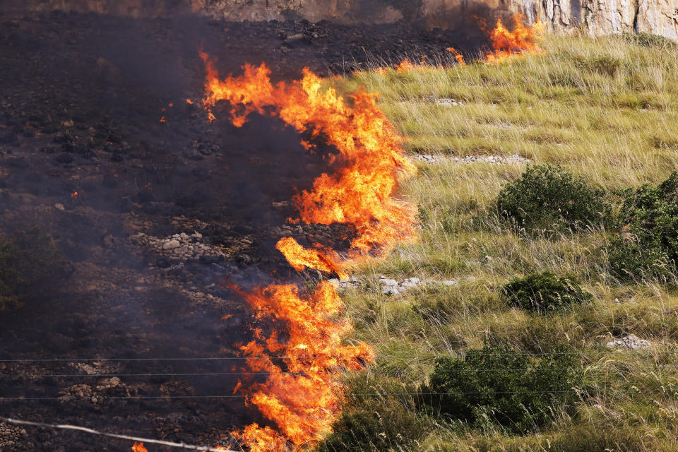 Flames burn in a field in Capaci, near Palermo, in Sicily, southern Italy, Wednesday, July 26, 2023. On the island of Sicily, two people were found dead Tuesday in a home burned by a wildfire that temporarily shut down Palermo's international airport, according to Italian news reports. Regional officials said 55 fires were active on Sicily, amid temperatures in the 40s Celsius. (Alberto Lo Bianco/LaPresse via AP)