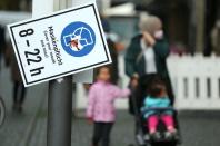 Pedestrians walk along a sign that reminds to wear a face mask as the coronavirus disease (COVID-19) outbreak continues in Frankfurt