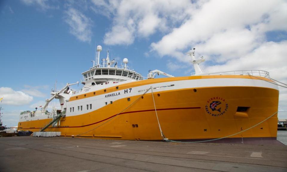 A very large, modern, handsome fishing trawler with a bright yellow hull and a white stripe at the dockside