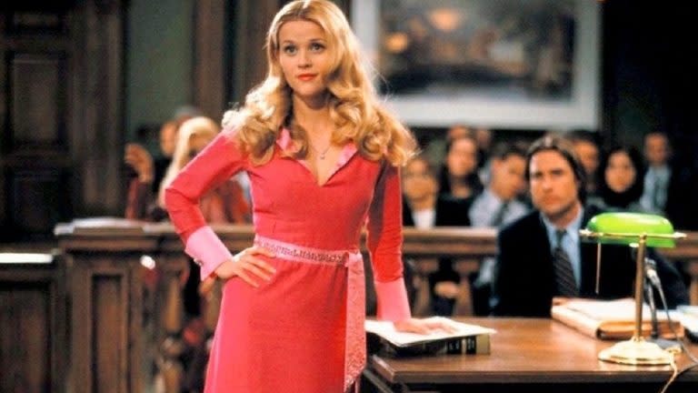 a photo of Elle Woods from Legally Blonde leaning on a desk wearing a bright pink dress