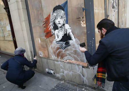 People photograph a new graffiti mural attributed to Banksy, opposite the French embassy in London, Britain January 25, 2016. REUTERS/Stefan Wermuth