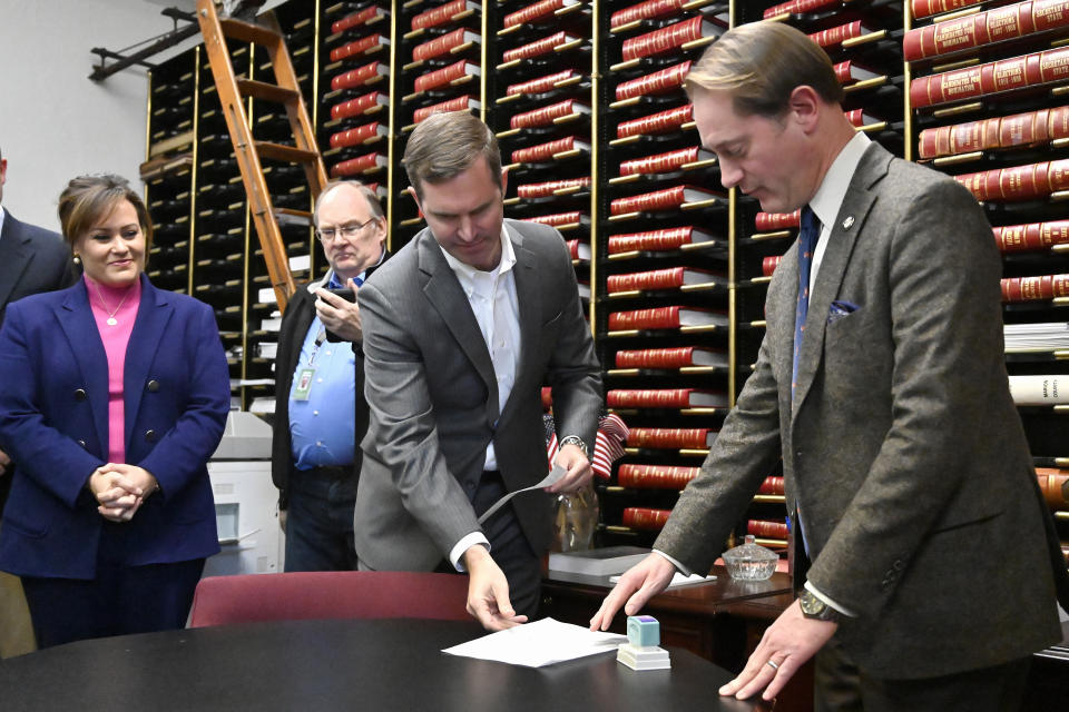 Kentucky Governor Andy Beshear, center, and Lt. Governor Jacqueline Coleman, left, presents the candidacy application to Secretary of State Michael Adams as he officially enters the race for reelection in Frankfort, Ky., Monday, Dec. 5, 2022. (AP Photo/Timothy D. Easley)