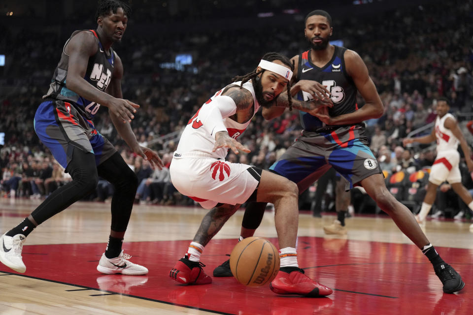 Toronto Raptors guard Gary Trent Jr., center, reaches for a loose ball under pressure from Brooklyn Nets forward Dorian Finney-Smith (28) and teammate Mikal Bridges (1) during the first half of an NBA basketball game in Toronto, Monday, March 25, 2024. (Nathan Denette/The Canadian Press via AP)