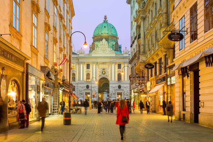 People stroll on a pedestrian street with shops leading to a domed building in the evening