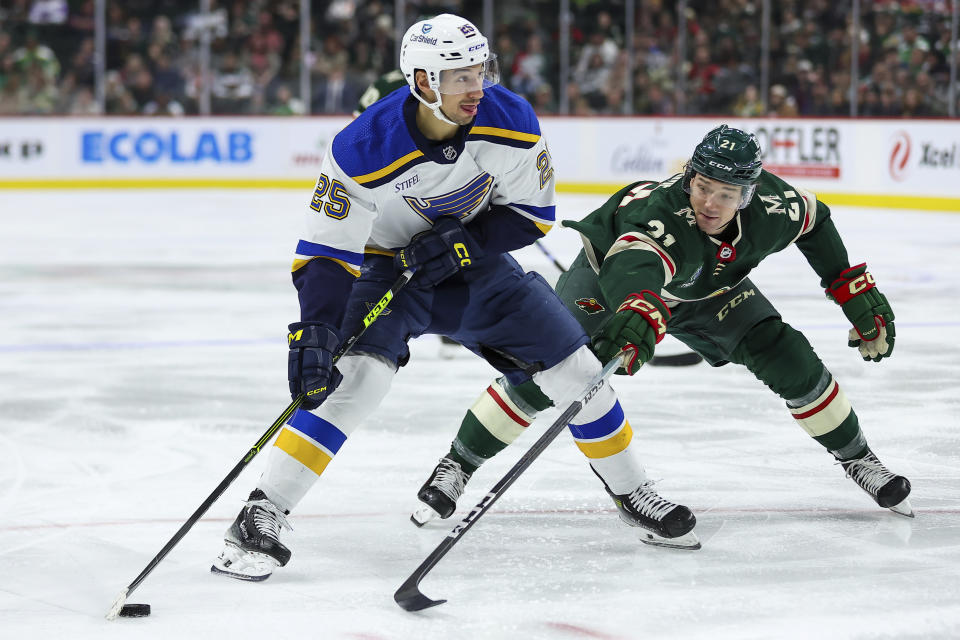 St. Louis Blues center Jordan Kyrou, left, skates with the puck alongside Minnesota Wild right wing Brandon Duhaime during the second period of an NHL hockey game ,Tuesday, Nov. 28, 2023, in St Paul, Minn. (AP Photo/Matt Krohn)