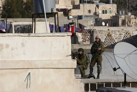 An Israeli soldier aims his weapon at Palestinians as Israeli settlers take over several houses, which are disputed between Palestinians and Israelis, in the West Bank old city of Hebron January 21, 2016. REUTERS/Mussa Qawasma