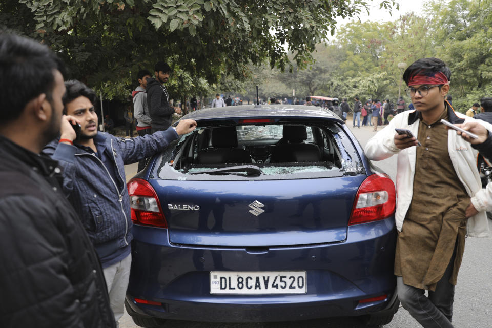 Students stand next to a car vandalized in Sunday's assault by masked assailants at the Jawaharlal Nehru University in New Delhi, India, Monday, Jan. 6, 2020. More than 20 people were injured in the attack opposition lawmakers are trying to link to the government. (AP Photo/Altaf Qadri)