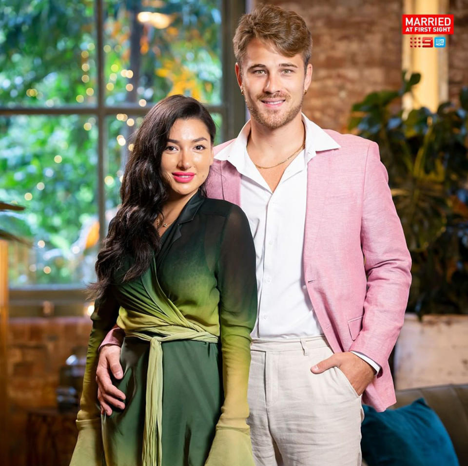 Ella Ding in a green dress posing with Mitchel Eynaud in a pink suit jacket, during filming of Married At First Sight 2022