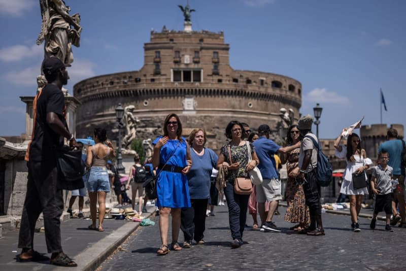 Tourists sturggle from the heat while crossing Ponte Sant Angelo. Italy is due to experience a heatwave in the coming days, with temperatures reaching nearly 40 degrees Celsius from Wednesday onwards, meteorologists predicted on 18 June. Oliver Weiken/dpa