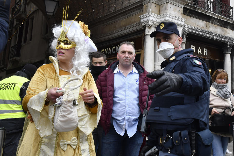 A policeman wearing a sanitary masks gestures next to a reveler in Venice, Sunday, Feb. 23, 2020. Italian authorities have announced they are shutting down Venice's famed carnival events in a bid to stop the spread of the novel virus, as numbers of infected persons in the country have soared to at least 133, the largest amount of cases outside Asia. (AP Photo/Luigi Costantini)