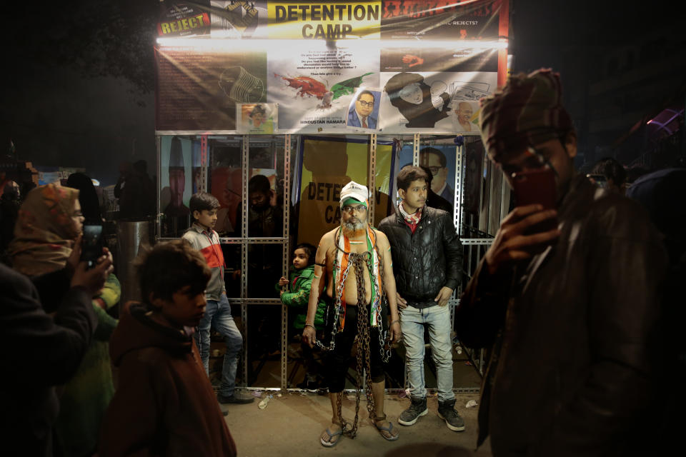 In this Tuesday, Jan. 21, 2020 photo, a Muslim man stands in shackles next to a mock detention camp at a protest site in New Delhi's Shaheen Bagh area, India. Muslim women are transcending the confines of their homes to lay claim to the streets of this nondescript Muslim neighborhood in the Indian capital and slowly transforming it into a nerve center of resistance against a new citizenship law that has unleashed protests across the country. The space is decorated with art and installations — from a mock detention camp to a mini replica of India Gate, Delhi’s famous World War I monument, inscribed not with the names of soldiers but of those killed in the nationwide protests. (AP Photo/Altaf Qadri)