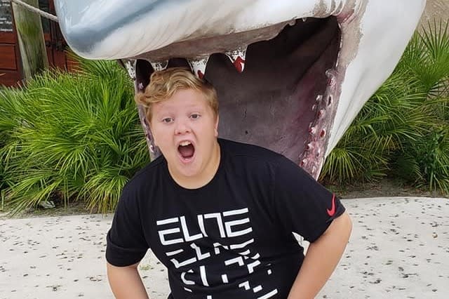 Peyton Baumgarth poses for a photo by putting his head between the jaws of a shark statue. 