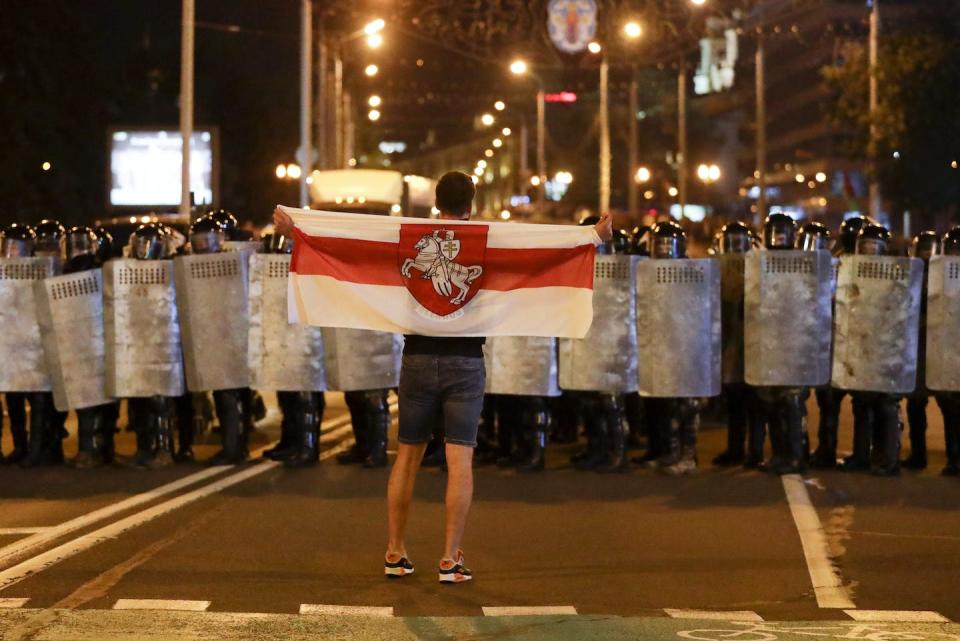 A protester holds an old Belarusian national flag as he stands in front of police line during a rally after the Belarusian presidential election in Minsk, Belarus, in August 2020. (AP Photo/Sergei Grits)