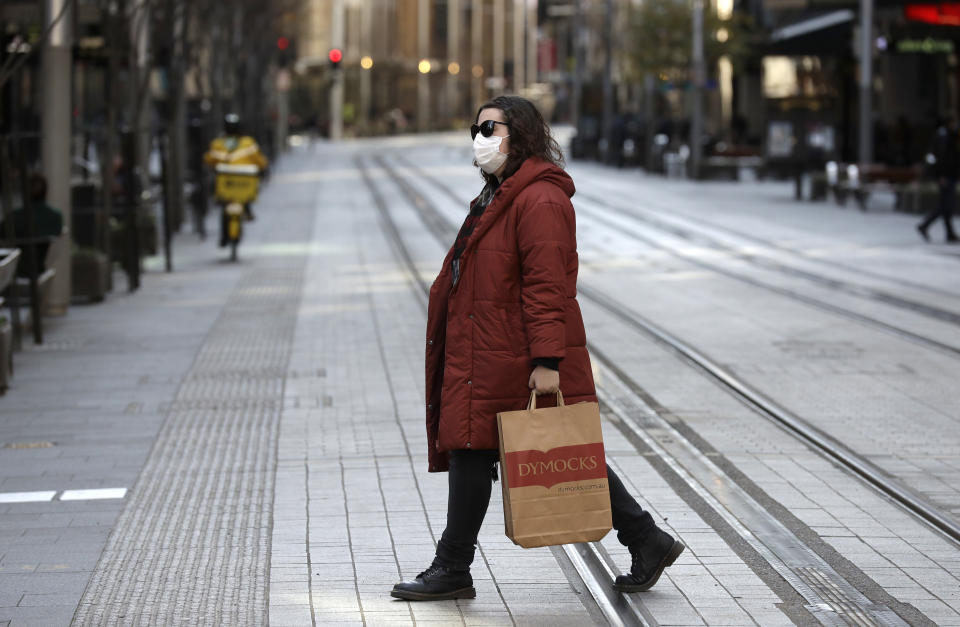 A woman crosses a normally busy street in Sydney, Wednesday, July 7, 2021. Sydney's two-week lockdown has been extended for another week due to the vulnerability of an Australia population largely unvaccinated against COVID-19, officials said. (AP Photo/Rick Rycroft)