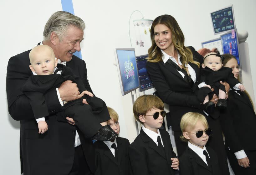 A man and a woman posing in matching black suits with a bunch of kids