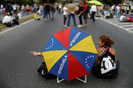 Opposition supporters covering themselves with an umbrella with the colours of the Venezuela's national flag, sit on a highway during a protest against Venezuelan President Nicolas Maduro's government in Caracas, Venezuela May 15, 2017. REUTERS/Carlos Garcia Rawlins