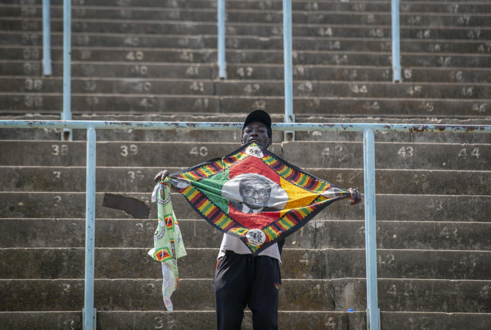 A man in the stands holds a banner with the face of former president Robert Mugabe, as members of the public queue up to view his body at the Rufaro stadium in the capital Harare, Zimbabwe Friday, Sept. 13, 2019. The ongoing uncertainty of the burial of Mugabe, who died last week in Singapore at the age of 95, has eclipsed the elaborate plans for Zimbabweans to pay their respects to the former guerrilla leader at several historic sites. (AP Photo/Ben Curtis)