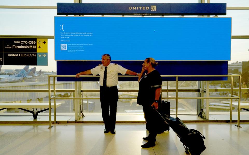 United Airlines staff wait by a departures monitor displaying the so-called 'blue screen of death, inside Terminal C in Newark International Airport, after United Airlines and other airlines grounded flights