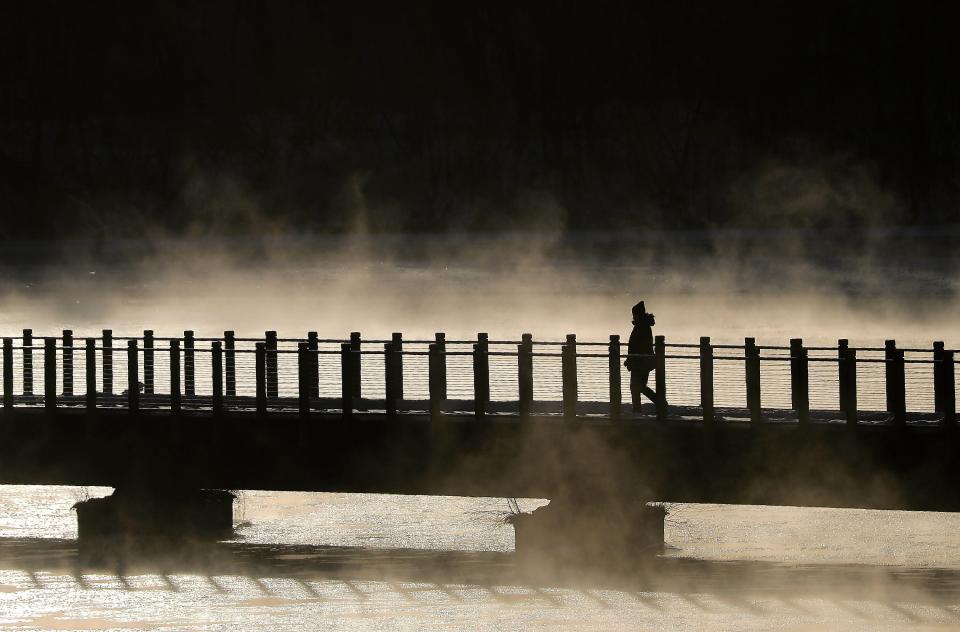 A person walks along the Lawe St. Trestle Trail  as the Fox River steams during frigid temperatures on Monday, January 10, 2022, in Appleton, Wis.