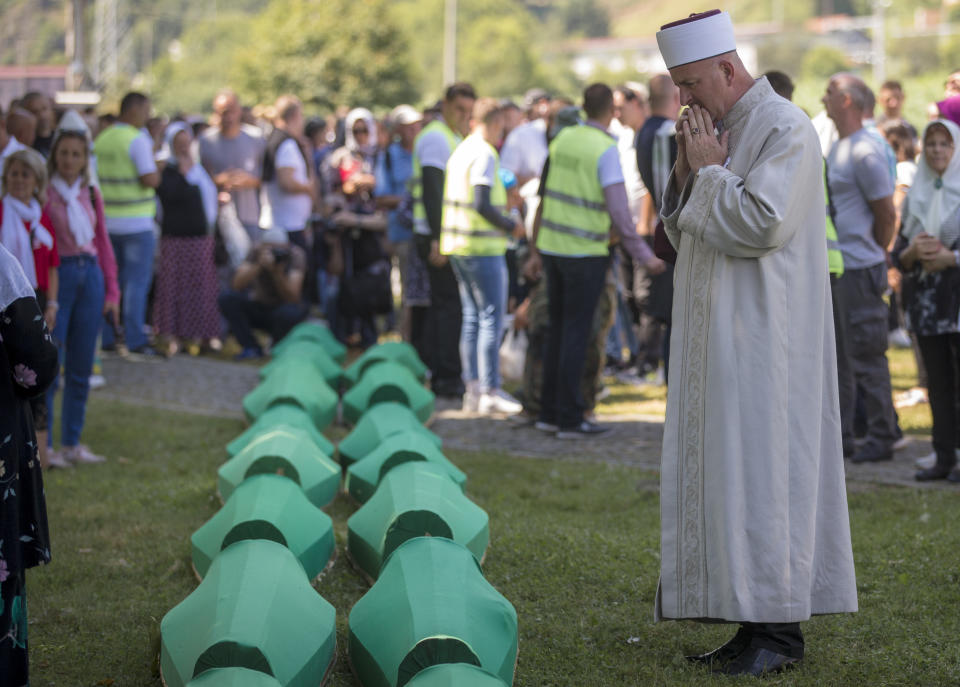 A cleric prays above coffins at the memorial cemetery in Potocari near Srebrenica, Bosnia, Thursday, July 11, 2019. The remains of the 33 victims of Srebrenica massacre will be buried 24 years after Serb troops overran the eastern Bosnian Muslim enclave of Srebrenica and executed some 8,000 Muslim men and boys, which international courts have labeled as an act of genocide. (AP Photo/Darko Bandic)