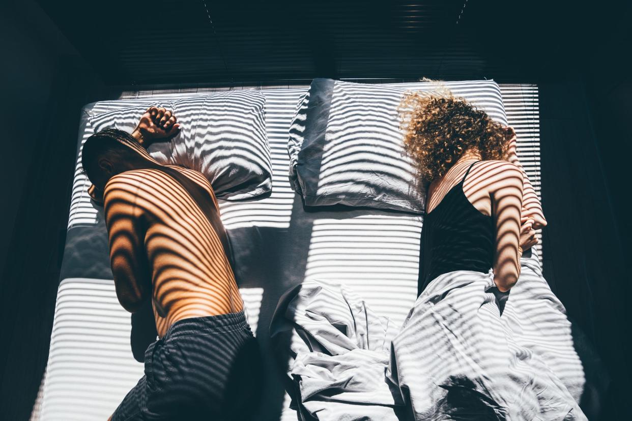 A man and woman lying on opposite sides of the bed facing away from each other.