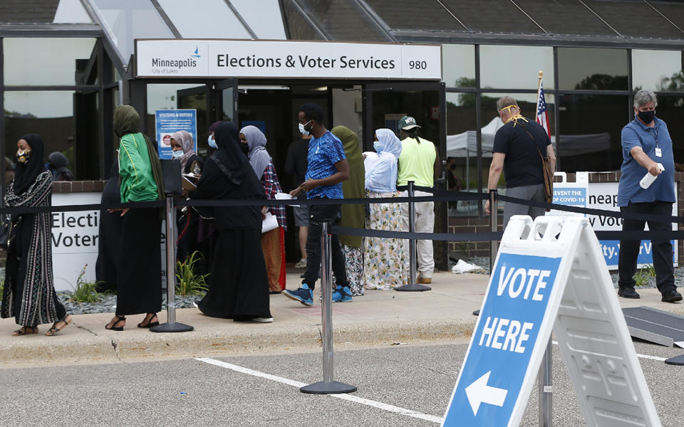 FILE - In this Aug. 10, 2020, file photo, Minneapolis voters line up to vote a day ahead of Minnesota's Tuesday primary election at the Minneapolis Election and Voters Services offices. A surge in coronavirus cases is hitting key presidential battleground states a little more than two weeks before Election Day, raising concerns that voting could be thrown into chaos despite months of preparation and planning by election officials and voters. (AP Photo/Jim Mone, File)