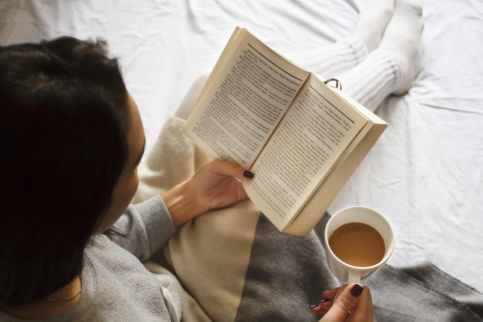 beautiful brunette girl reading book and drinking coffee in bed in the morning