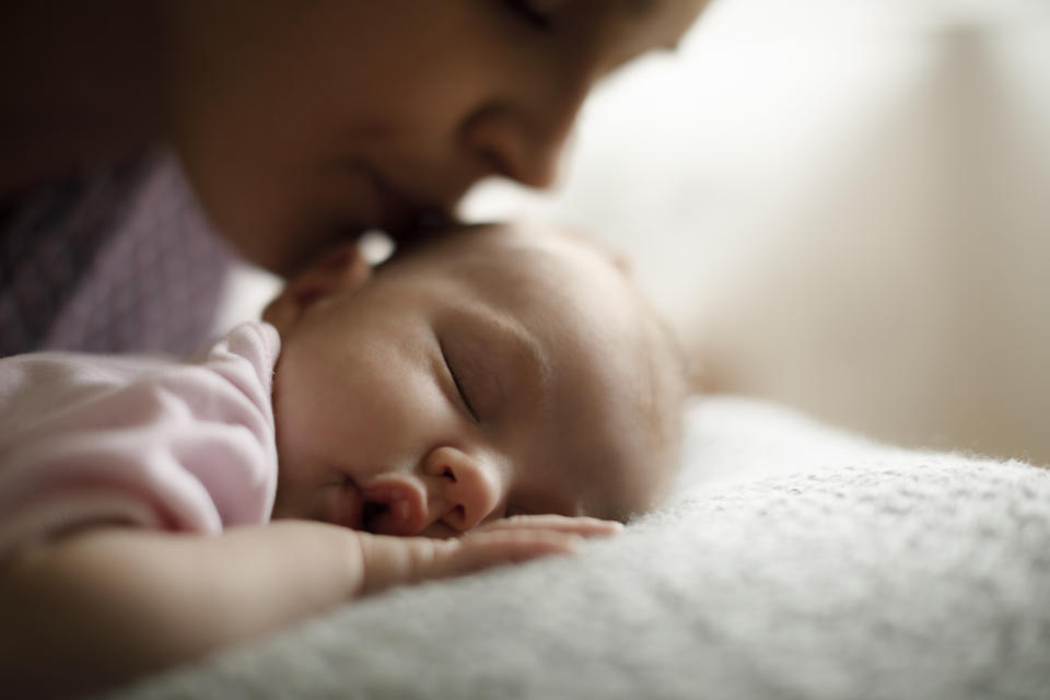 Parent gently kissing their sleeping infant's head