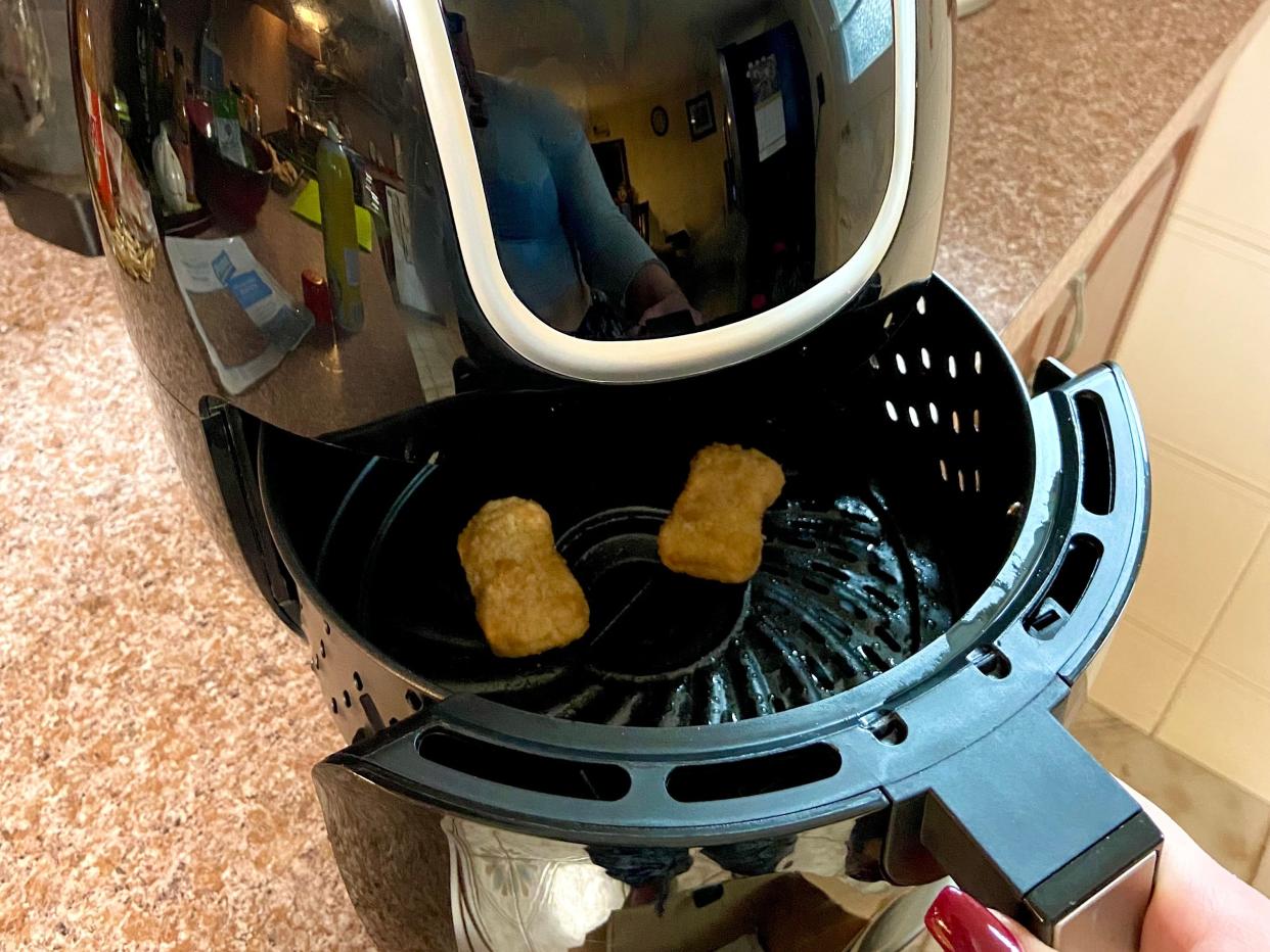 An air fryer basket with two nuggets being placed into the full air fryer appliance.