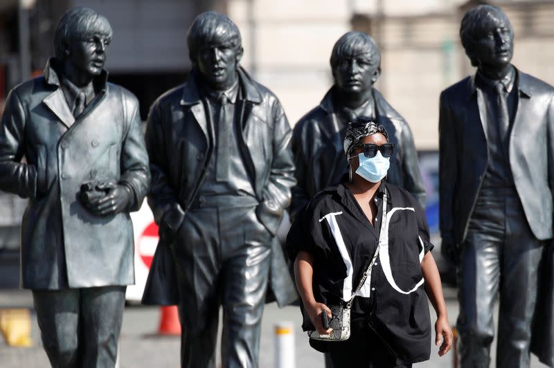 A woman wears a face mask as she stands in front of a statue of The Beatles in Liverpool