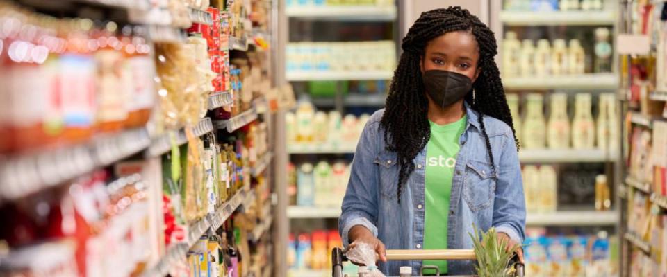 Woman shopping in an Instacart t-shirt in a grocery store, wearing mask.