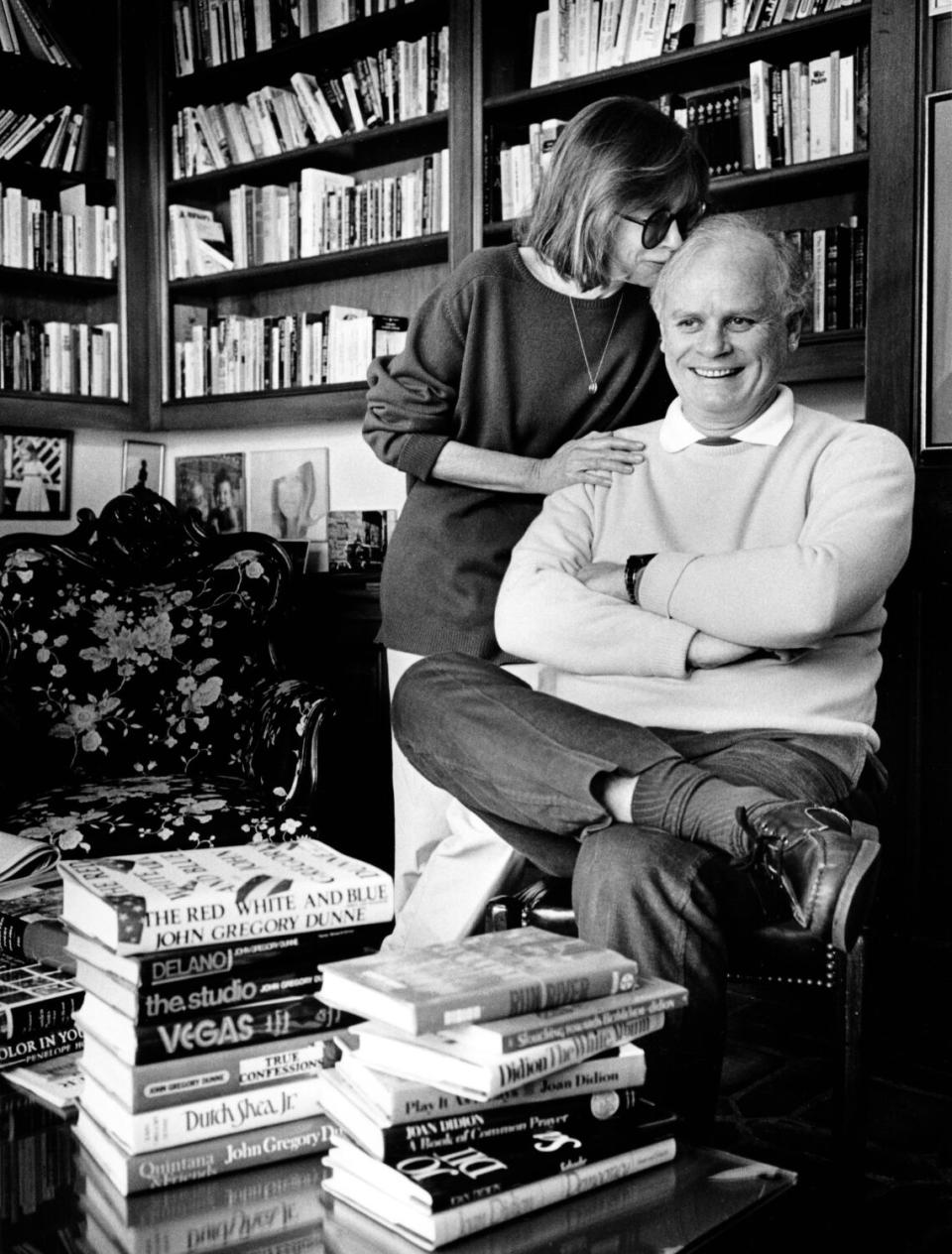 black and white photo of a woman standing kissing a sitting man on the head, surrounded by books