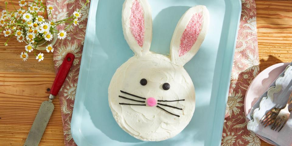 a single layer cake shaped like the easter bunny's head with tall ears and eyes and a nose and whiskers