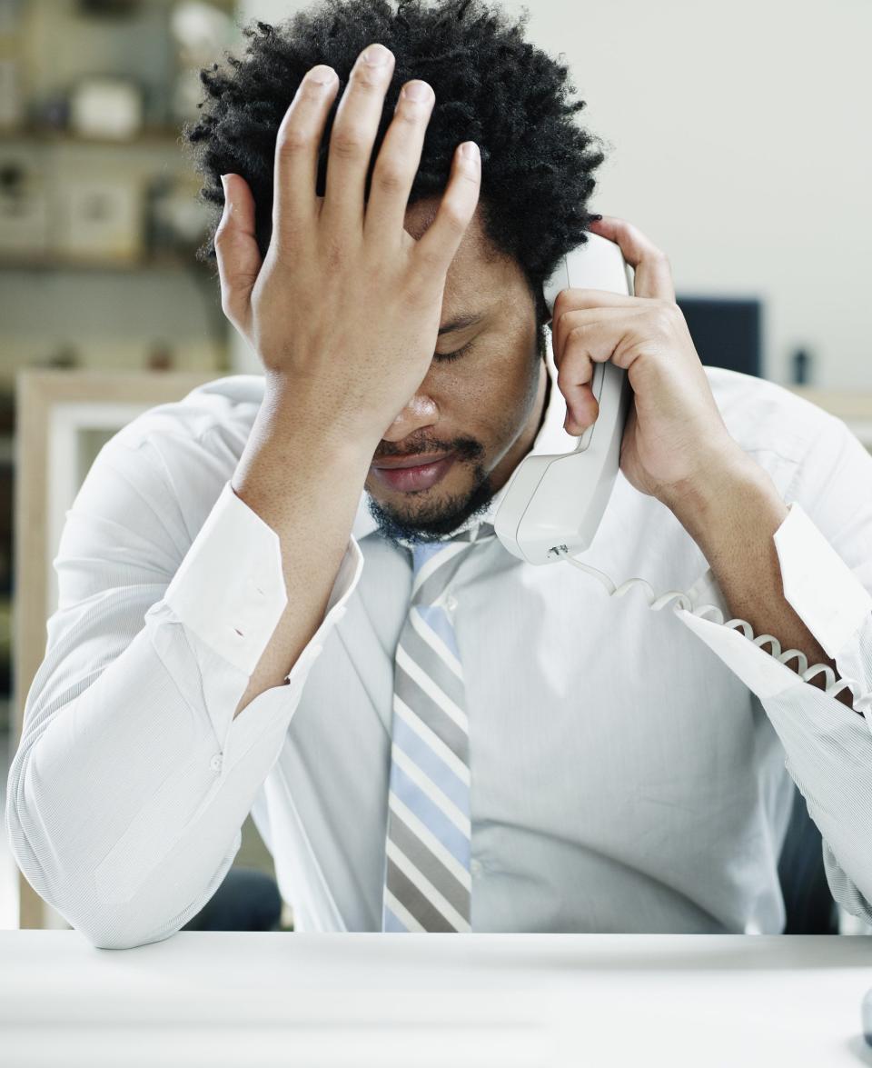 A man holds his hand to his forehead in frustration during an emotional phone call