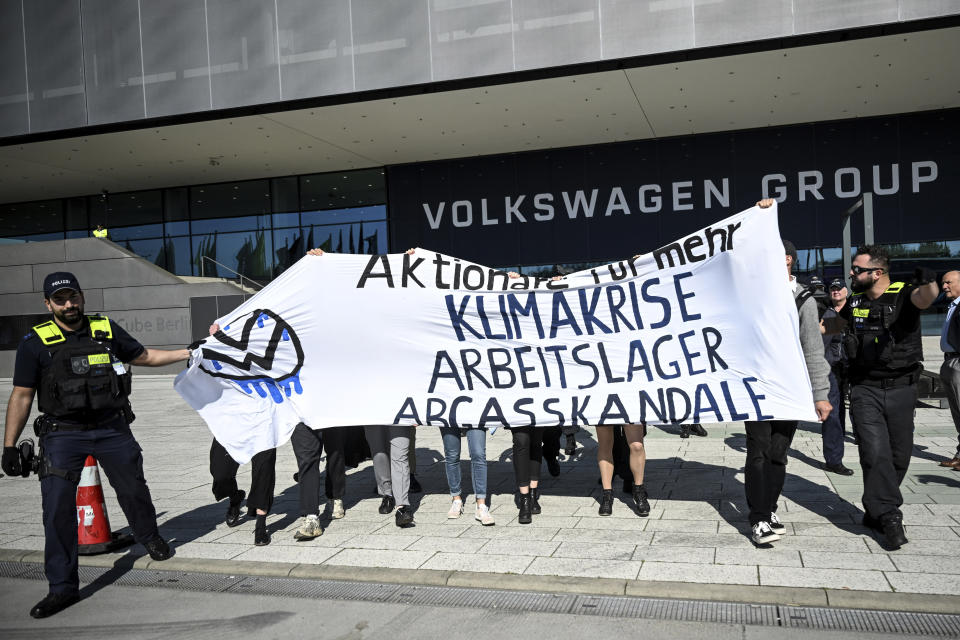 Climate activists hold a protest banner outside the annual shareholders' meeting of the Volkswagen AG in Berlin, Germany, Wednesday, May 10, 2023. Slogan reads: 'Shareholders' for more Climate Crises, Labour Camps, Emissions Scandals'. (Britta Pedersen/dpa via AP)