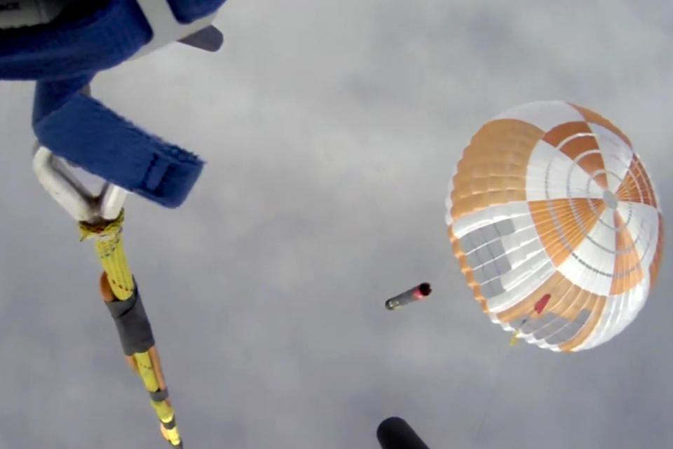 In this image made from video supplied by Rocket Lab, a helicopter hovers above as it attempts to capture Electron's first stage in mid-air by helicopter above New Zealand, Tuesday, May 3, 2022. Rocket Lab launched its rocket from their launch pad on the Mahia Peninsula. The California-based company regularly launches 18-meter (59-foot) rockets from the remote Mahia Peninsula in New Zealand to deliver satellites into space. (Rocket Lab via AP)