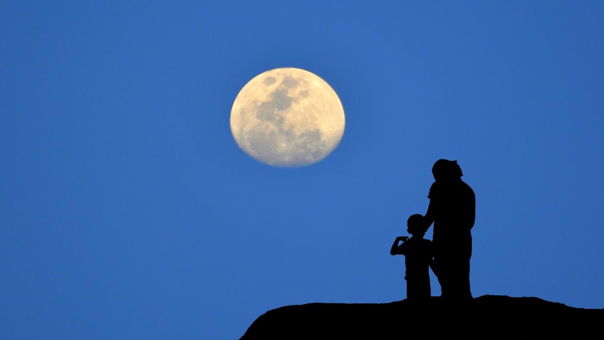  Silhouette of mother and child watching the moon against the blue night sky. 