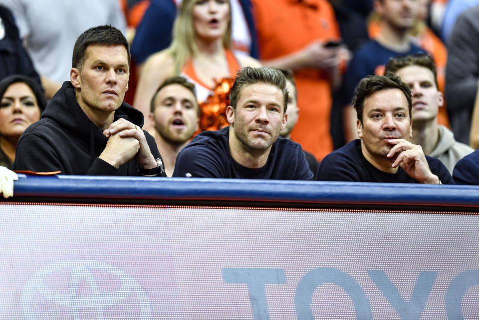 New England Patriots' Tom Brady, left, and Julian Edelman, center, along with comedian Jimmy Fallon watch from the sidelines during the first half of an NCAA college basketball game between Syracuse and North Carolina in Syracuse, N.Y., Saturday, Feb. 29, 2020. (AP Photo/Adrian Kraus)